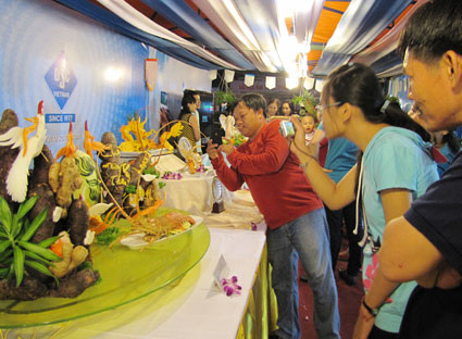 Khách tham quan thích thú chụp ảnh các tác phẩm nghệ thuật từ rau củ trưng bày tại Lễ hội ẩm thực phố biển.