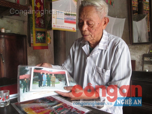 Ông Trương Đắc Suê bên những tấm ảnh                    trong lễ biểu dương