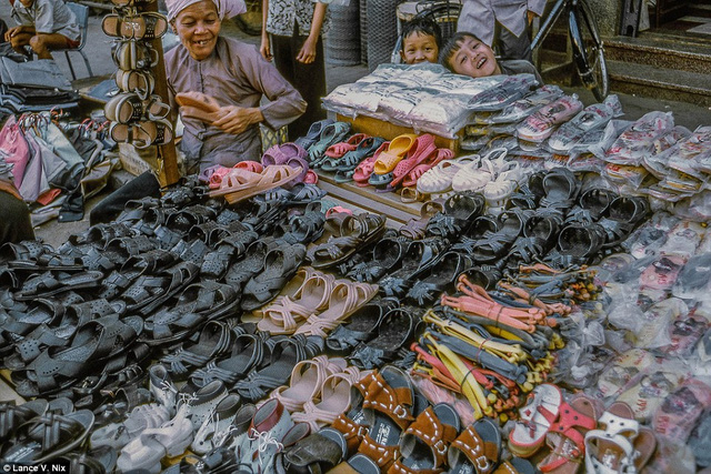 Người đàn bà bán dép cùng hai đứa trẻ tươi cười khi ống kính hướng vào họ.