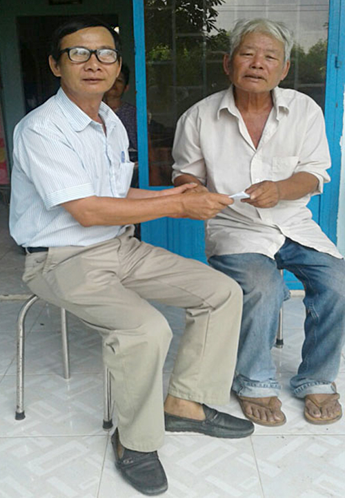 Ông Vũ Kim Bàn (trái) trao phiếu nhận quà cho ông Phạm Đức Tùng (ấp 5, xã Tóc Tiên) có mẹ, vợ và em trai bị liệt. 