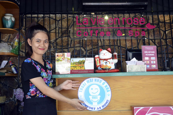 Chị Đoàn Thị Phương Dung, nhân viên quán Coffee & Spa La Vie en Rose (6, Hạ Long, TP.Vũng Tàu) giới thiệu logo nhận diện mô hình NVS cộng đồng “Thoải mái như ở nhà - Comfort as home” được dán tại quán.