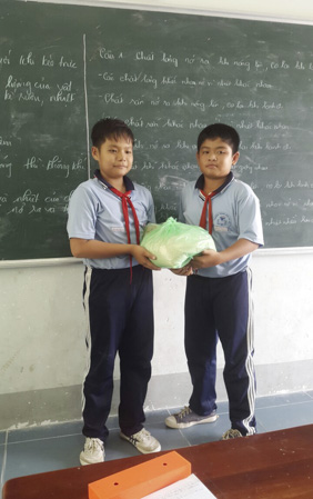 Em Đặng Vô Biên, lớp trưởng lớp 6A (trái) trao tặng gạo cho bạn Nguyễn Thanh Sang, HS có hoàn cảnh khó khăn của lớp.
