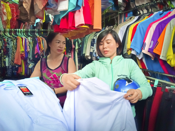 Chị Thu Hà (trái), tiểu thương chợ Rạch Dừa tư vấn cho khách hàng chọn mua đồng phục học sinh.