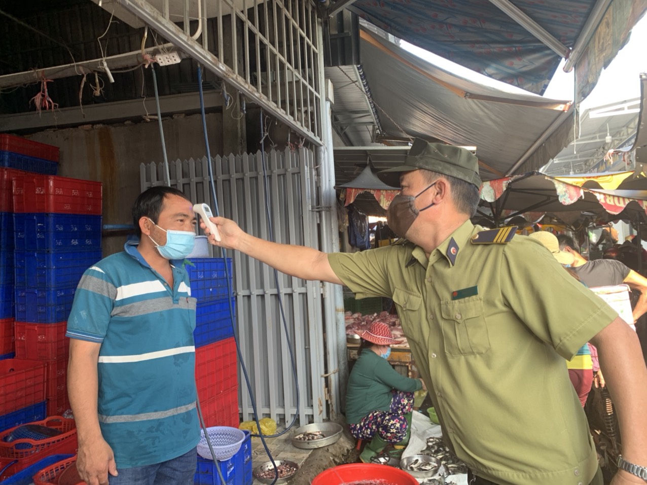 Nhân viên Ban Quản lý chợ TT. Phước Bửu (huyện Xuyên Mộc) kiểm tra thân nhiệt tiểu thương kinh doanh hải sản. Ảnh: HUYỀN TRANG