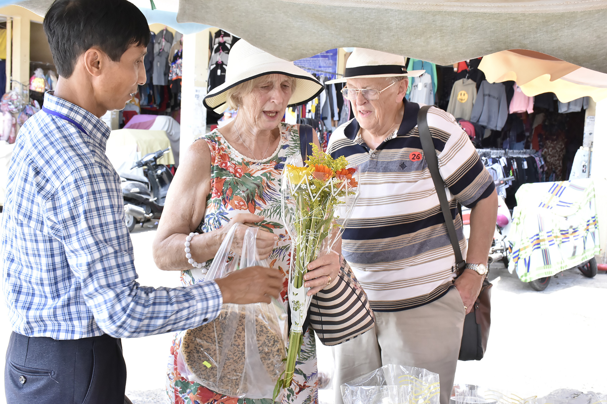 Sau một vòng dạo chợ Hòa Long, 2 du khách Anh mua bánh tráng, hoa tại chợ.
