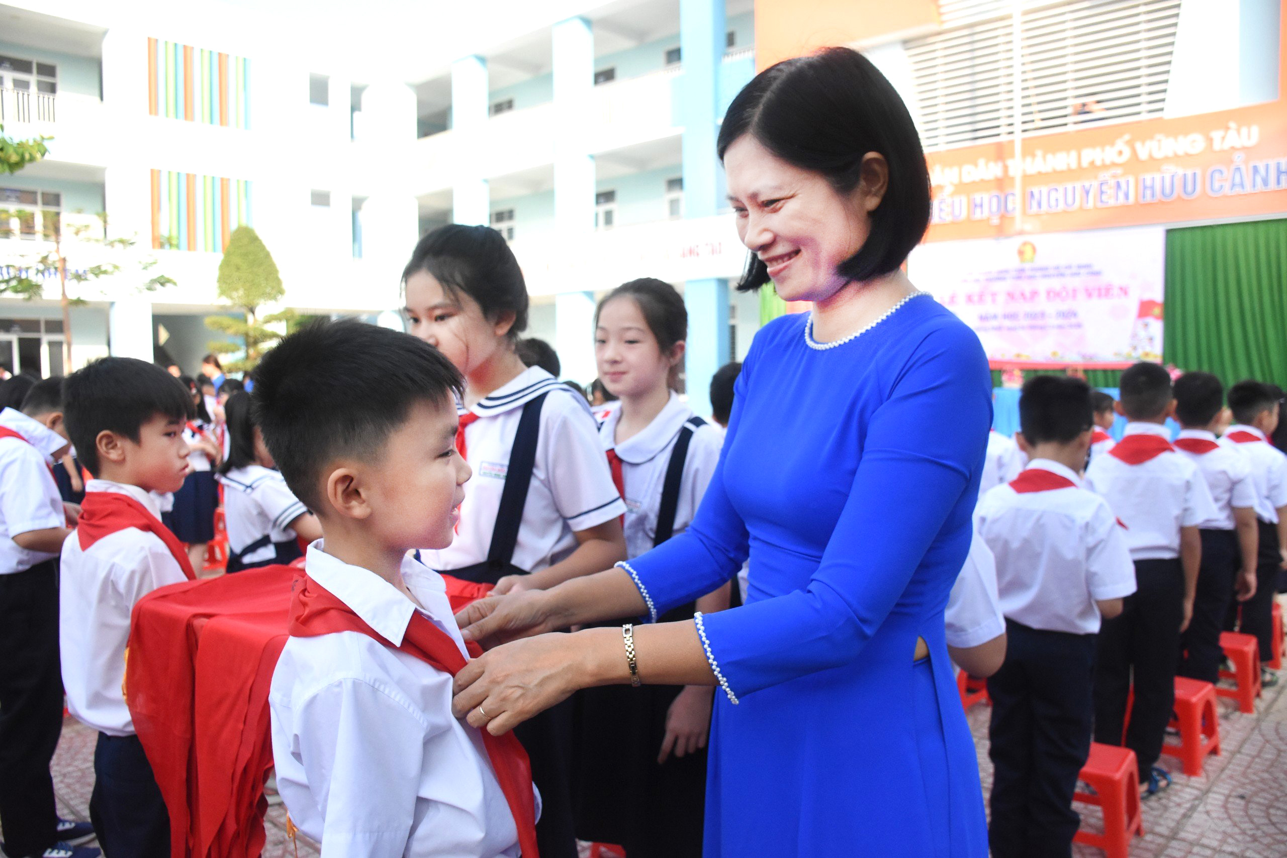 Cô Trần Thị Nhàn, Bí thư Chi bộ, Hiệu trưởng Trường TH Nguyễn Hữu Cảnh trao khăn quàng cho HS trong lễ kết nạp Đội viên.