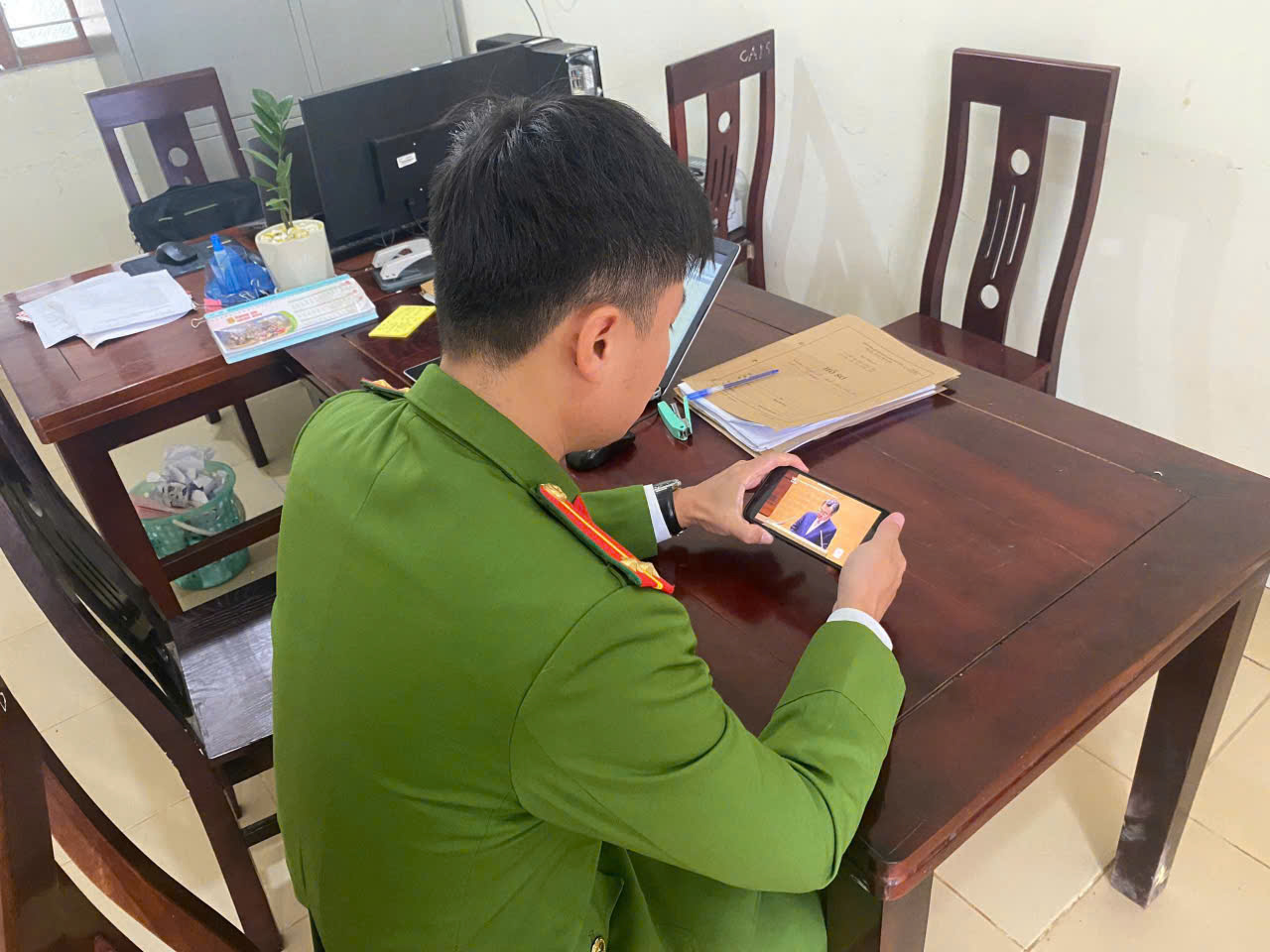 Cán bộ Công an xã Anh Sơn chăm chú theo dõi truyền hình trực tiếp Hội nghị qua điện thoại di động