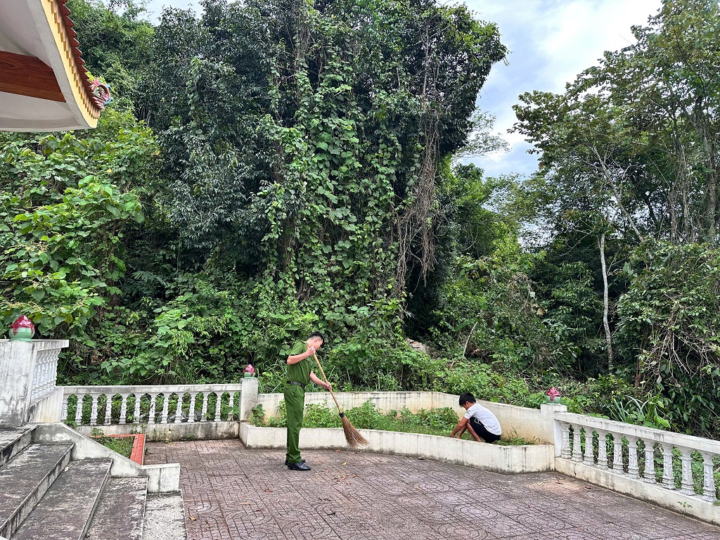 Công an xã và học sinh tham gia quét dọn, nhổ cỏ khuôn viên Nhà bia tưởng niệm các Anh hùng liệt sĩ