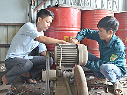 Anh Nguyễn Minh Châu (bìa phải) hướng dẫn công nhân sử dụng máy cắt tại xưởng cơ khí Minh Châu.