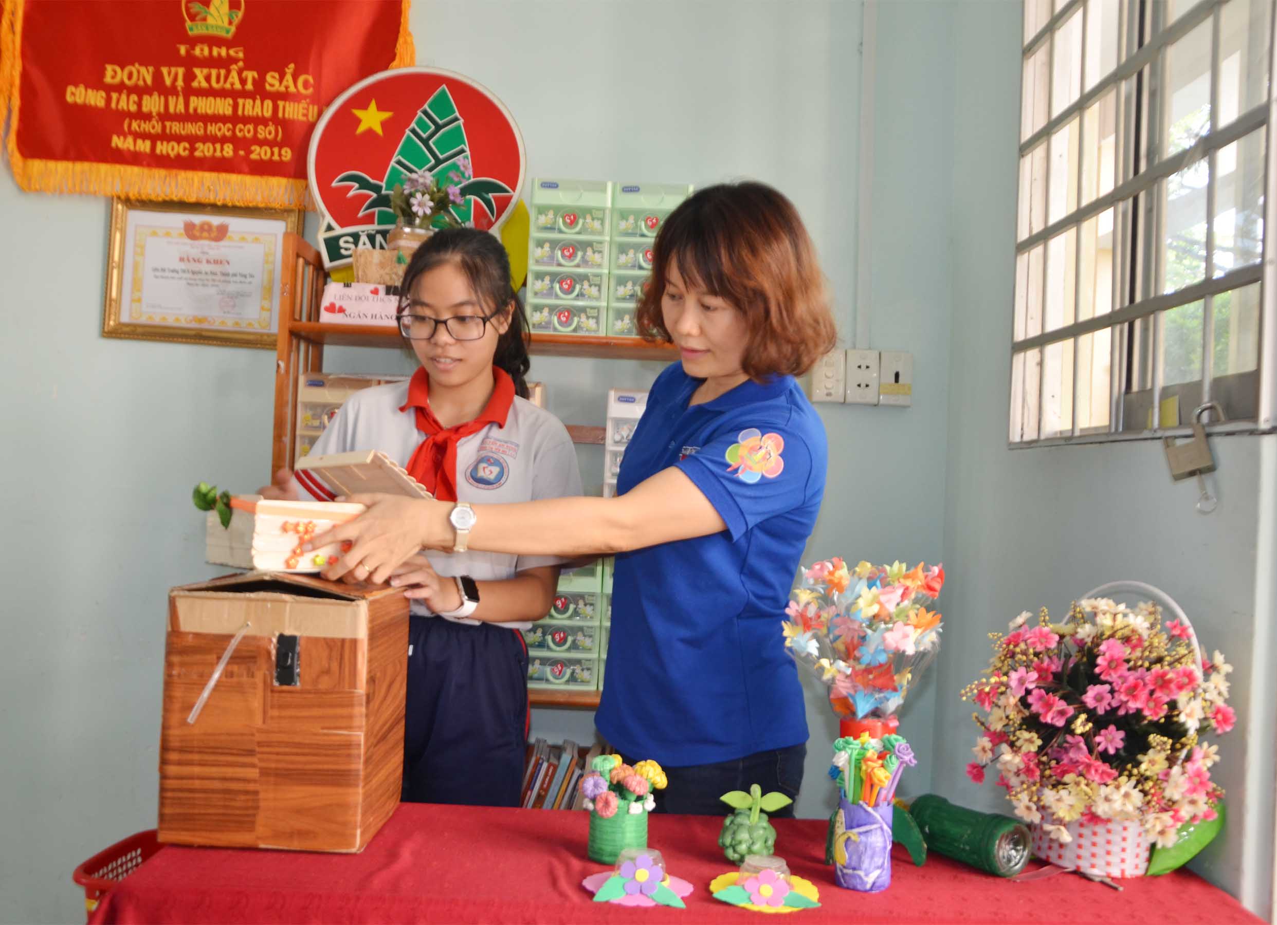 Yến Nhi và cô Tổng phụ trách Đội Lê Thị Thúy Hằng chuẩn bị các sản phẩm sáng tạo Khoa học-Kỹ thuật của HS trong trường để gửi đi dự thi.