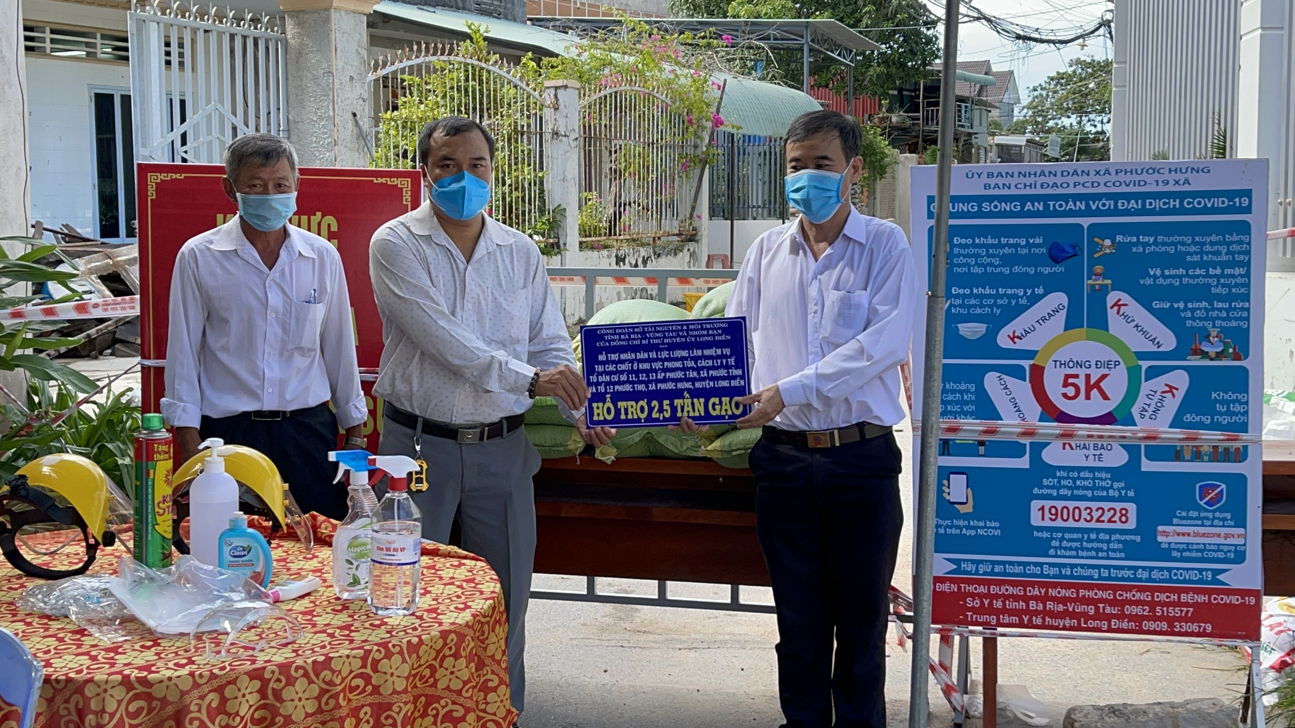 Ông Huỳnh Minh, Chủ tịch UBMTTQ huyện (bìa phải) trao bảng tượng trưng hỗ trợ gạo cho địa phương tại chốt phong tỏa, cách ly.