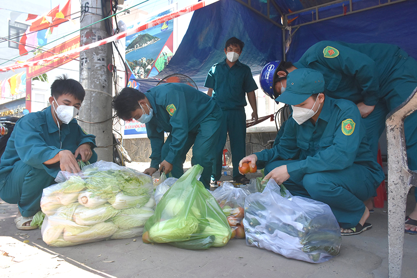 Lực lượng dân quân hỗ trợ sắp xếp rau vào bịch để mang đến cho người dân Long Hải. Ảnh: HUY ANH
