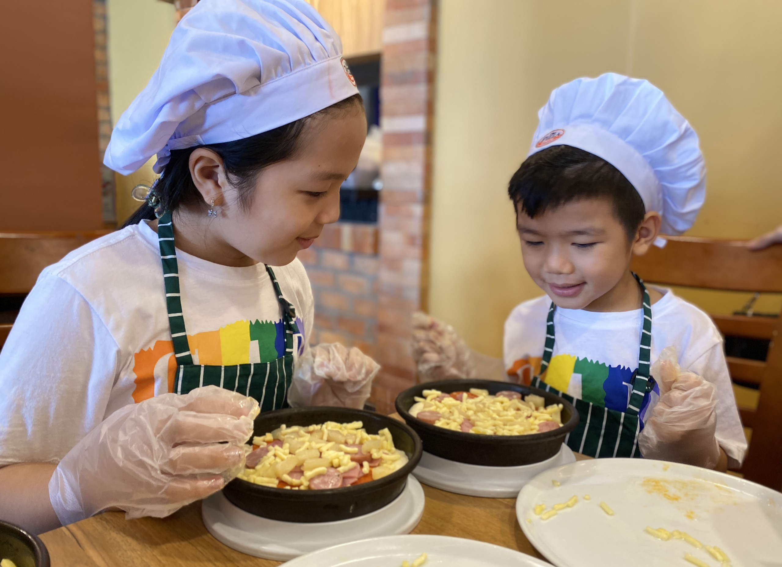 Hai em bé trang trí bánh pizza do chính tay mình làm.