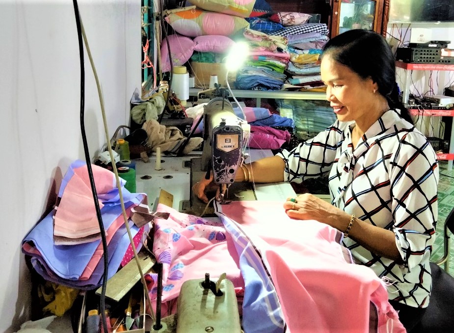 Chị Lê Yến Tuyết bên chiếc máy may cùng với sản phẩm là chăn, ga, mền đa dạng mẫu mã được người dân địa phương ưa chuộng.
