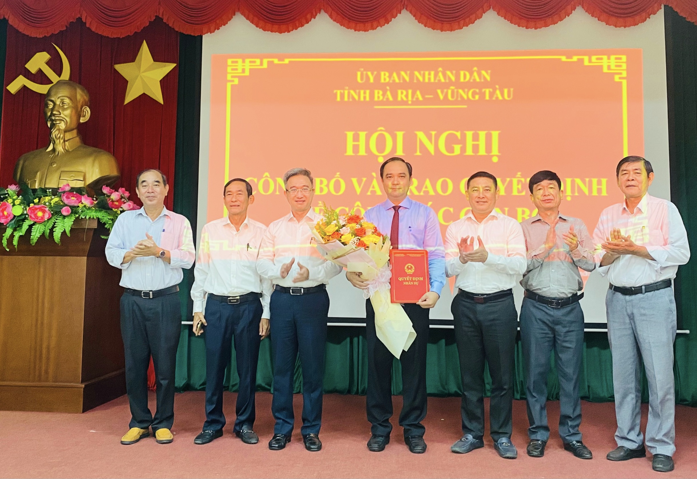 Ông Đặng Minh Thông (thứ 3 từ trái qua), Phó Chủ tịch UBND tỉnh; ông Huỳnh Sơn Tuấn (thứ 3 từ phải qua), Bí thư Huyện ủy Long Điền trao quyết định và tặng hoa chúc mừng ông Lê Hữu Hiền.