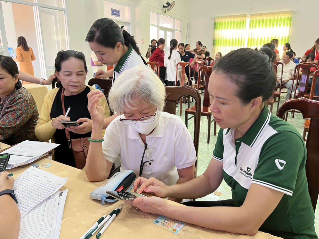 Nhiều người dân trên địa bàn phường 2 có mặt từ sáng sớm để được hỗ trợ cài đặt các dịch vụ trực tuyến. Trong ảnh: Ngân hàng Vietcombank hỗ trợ người dân cài đặt aap.