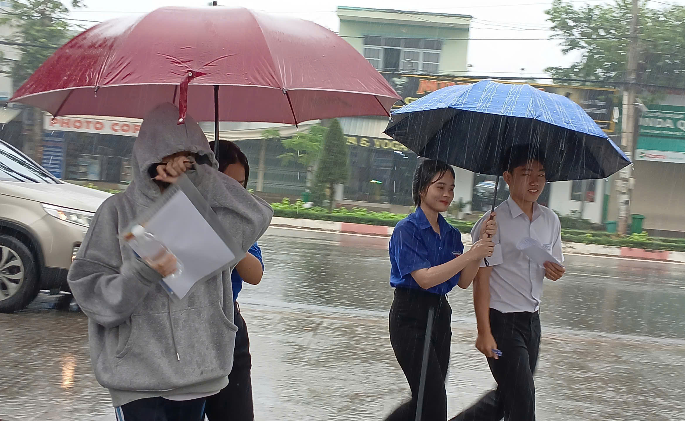 Tình nguyện viên tại điểm thi Trường THPT Hắc Dịch (TP.Phú Mỹ) che ô giúp thí sinh di chuyển vào phòng thi.