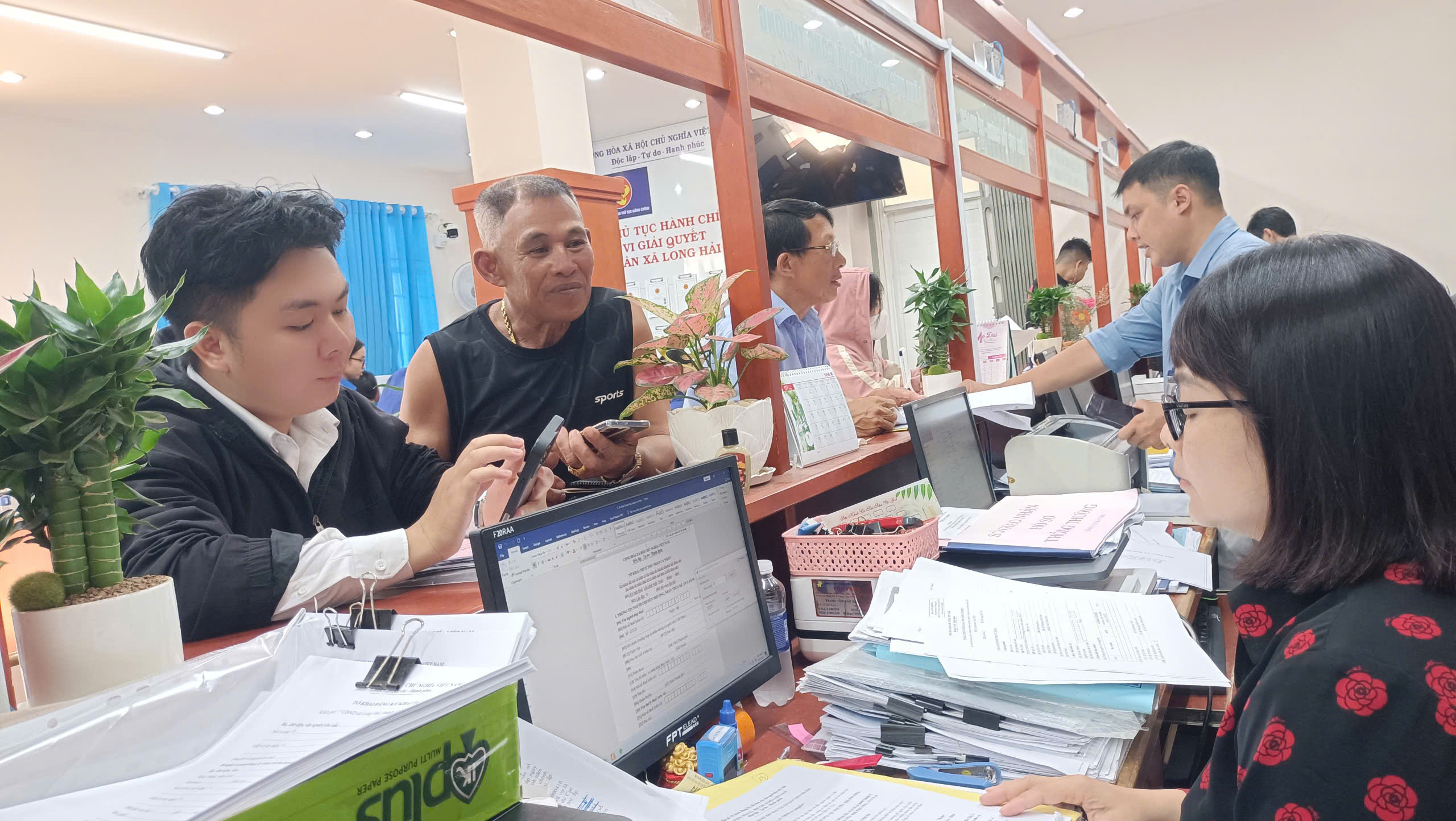 Hiện mỗi ngày xã Long Hải tiếp nhận khoảng 250 hồ sơ, thủ tục hành chính của người dân, tất cả đều được số hóa và phần lớn thực hiện trực tuyến qua cổng dịch vụ công. Trong ảnh: Cán bộ xã Long Hải hướng dẫn người dân thực hiện nộp hồ sơ đăng ký đất đai qau App điện thoại. Ảnh: Ngọc Minh.